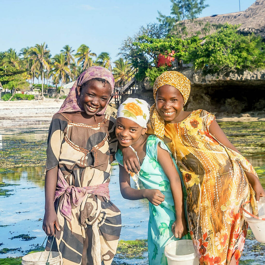 Young African girls collecting shells near Rock restaurant in Zanzibar